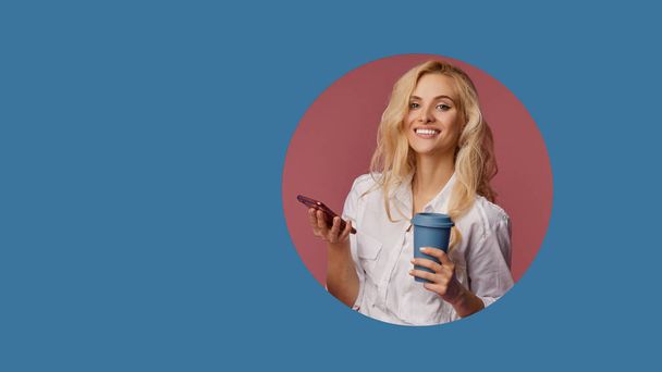 Portrait of a satisfied young woman using mobile phone while holding cup of coffee to go. Peeping of the classic blue circle hole in the wall. Making selfie and smiling  - Fotó, kép