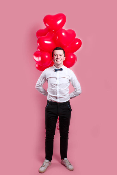 Elegante jongeman met hartvormige luchtballonnen op roze achtergrond. Valentijnsdag. - Foto, afbeelding