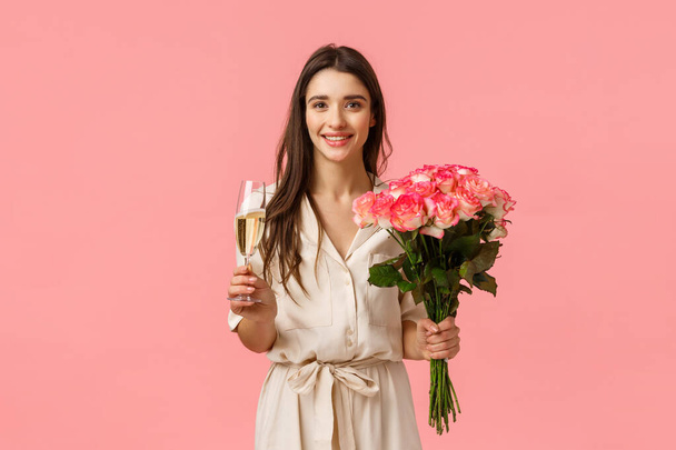 Oslava, romantika a koncept vztahu. Svůdná krásná žena slaví a paří, obdrží krásné kytice, drží květiny růží a skleněné šampaňské, růžové pozadí - Fotografie, Obrázek