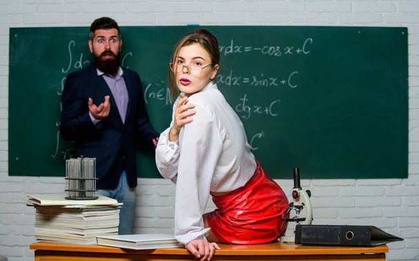 Attractive teacher in leather skirt. Cheeky teacher. Impudent student. Flirting with colleague. Science is sexy. Sexy girl sit table while man stand chalkboard. Everyone dreaming about such teacher - Fotografie, Obrázek