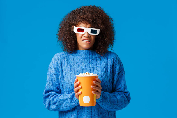 Uneasy et triste femme afro-américaine mignonne avec coupe de cheveux afro regarder personnage préféré mourir dans le film, grimaçant bouleversé et affligé, porter des lunettes 3D fronçant les sourcils au cinéma, manger du maïs soufflé
 - Photo, image