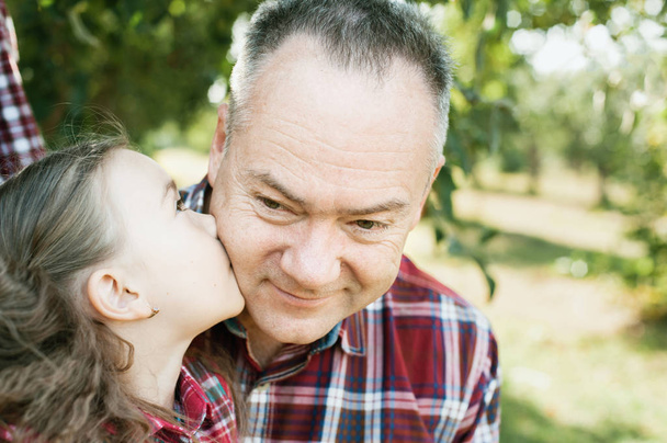 εγγονή φιλιά στο μάγουλο παππού, ενώ απολαμβάνουν στο πάρκο άνοιξη  - Φωτογραφία, εικόνα