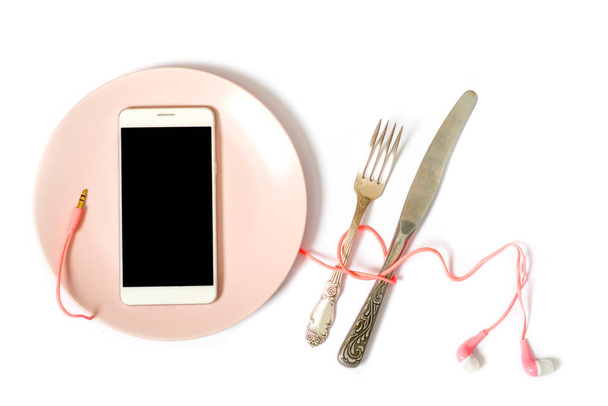 Telefon auf einem rosa Teller, Ohrstöpsel auf einem Teller. Konzept der Gadgets beim Essen - Foto, Bild