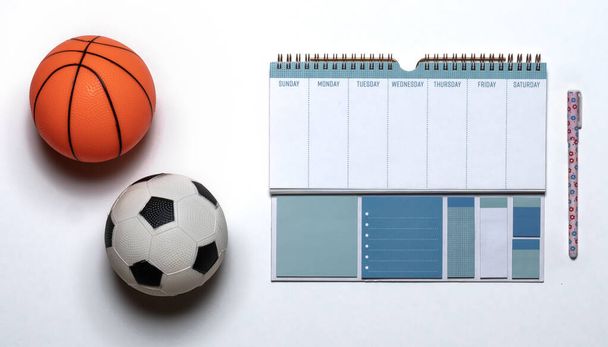 Pequeño juguete de goma de baloncesto y pelota de fútbol con un calendario de plan de entrenamiento
 - Foto, Imagen