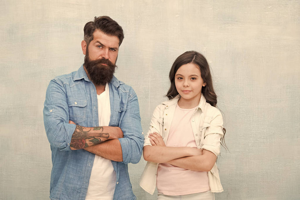 Casual appeal. Small girl and bearded man in casual style on grey background. Casual look of father and little daughter. Cute child and brutal hipster keeping arms crossed in casual wear - 写真・画像