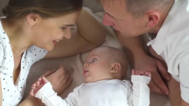 Happy family. Mom dad and three month old baby. Family lying in bed and looking at the camera, smiling. - Footage, Video