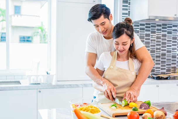Asiáticos parejas cocinar y rebanar verduras en la cocina juntos
. - Foto, imagen