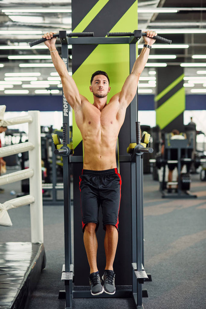 Attractive man does pull-up on the crossbar during training in the modern gym. Front view. - Fotografie, Obrázek