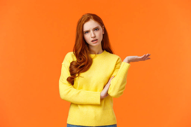 Skeptical and troubled, uncertain young redhead woman cant understand how resolve proble, shrugging raise hands sideways, frowning confused or unsure, standing frustrated orange background - Photo, Image