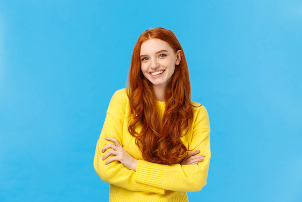 Waist-up shot fashionable pretty hipster girl with red hair, blue eyes, freckles, smiling lovely with cheerful expression, hold hands crossed over chest, confident professional pose, blue background - Photo, image