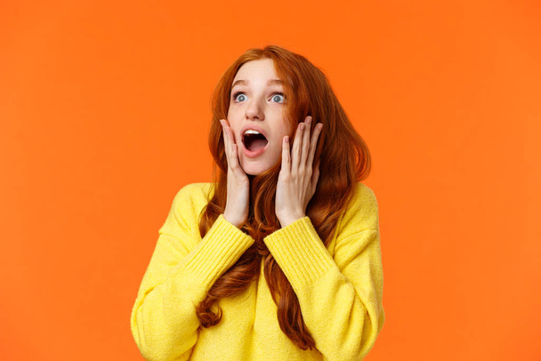 Oh no something falling from sky. Shocked and speechless, startled young concerned redhead woman drop jaw, gasping and staring upper left corner concerned, touching face worried, orange background - Foto, Imagen