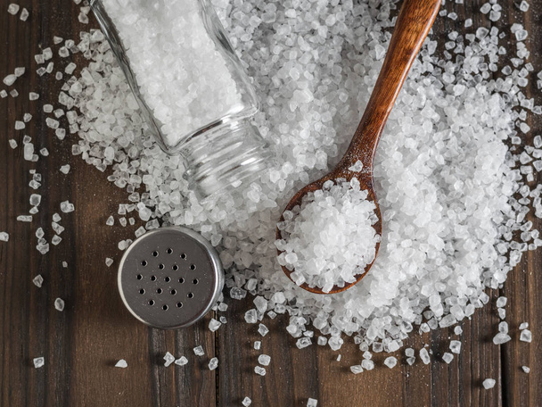 Roztroušená velká mořská sůl s dřevěnou lžící a solným třepačem. - Fotografie, Obrázek