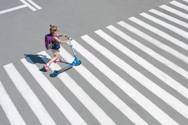 Girl carrying scooter and crossing road on way to school - Foto, Imagen