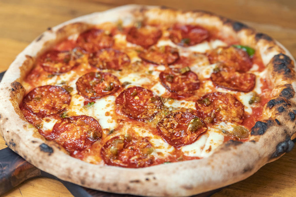Свежеиспечённая пицца с салями, сыром, соусом, овощами и мясом на деревянном столе
 - Фото, изображение