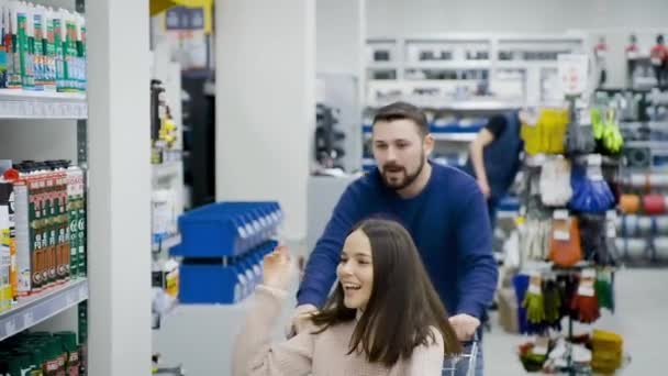 Guy rolls jeho atraktivní mladá přítelkyně v vozíku v supermarketu. - Záběry, video