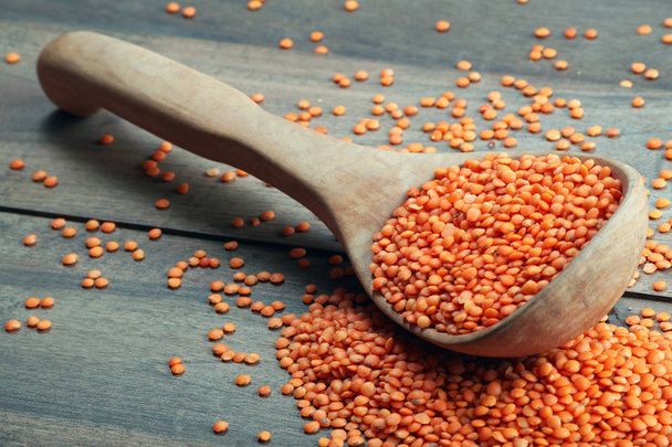 red lentils in a wooden spoon on a wooden table. close up - Zdjęcie, obraz
