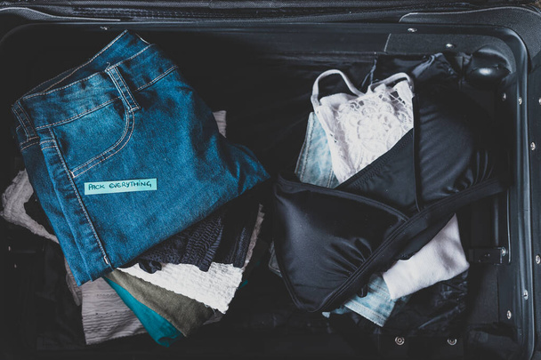 luggage with pile of clothes and Packing Everything label on the - Foto, imagen