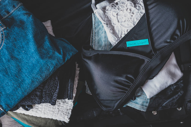 luggage with few clothes inside and Packing Light label on them - 写真・画像