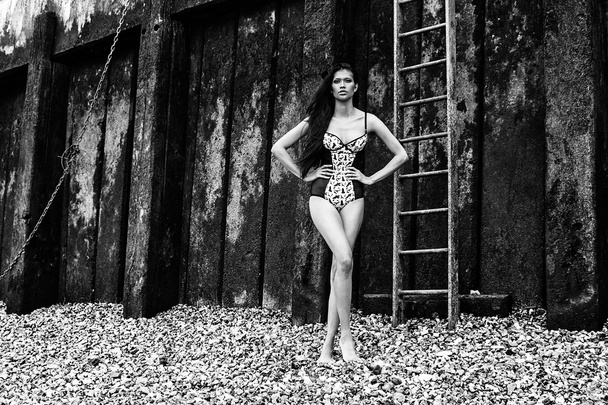 Белье бикини молодая сексуальная латиноамериканская фотомодель позирует на пляже рядом со старой грязной стеной
 - Фото, изображение