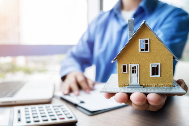Модель дома на руку агента, который показывает клиентам, чтобы купить, получить страховку, кредит недвижимости или собственности. - Фото, изображение