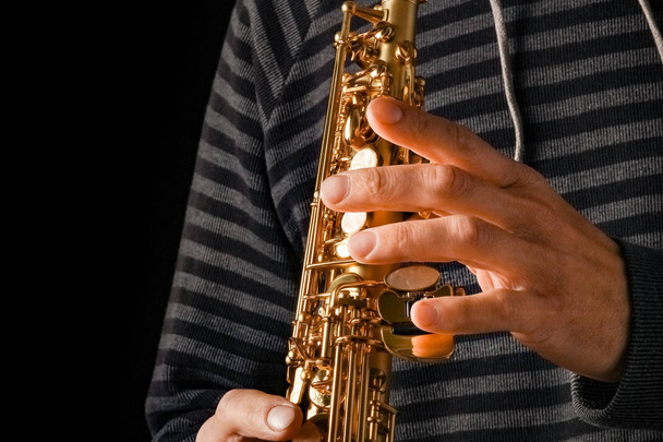 soprano saxophone in the hands of a guy on a black background - Zdjęcie, obraz