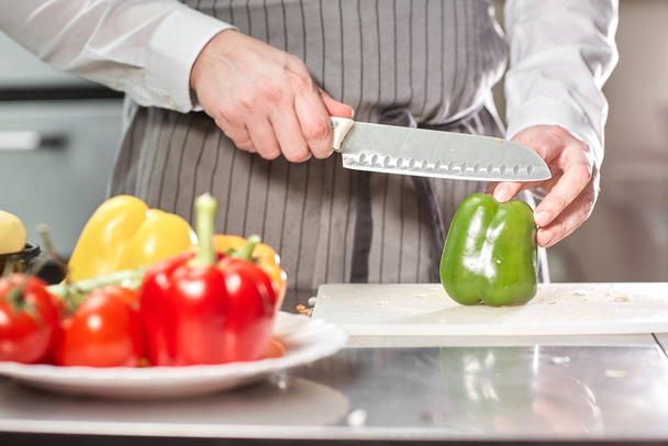 Closeup of hand with knife cutting fresh vegetable. Young chef cutting beet on a white cutting board closeup. Cooking in a restaurant kitchen - Foto, Bild