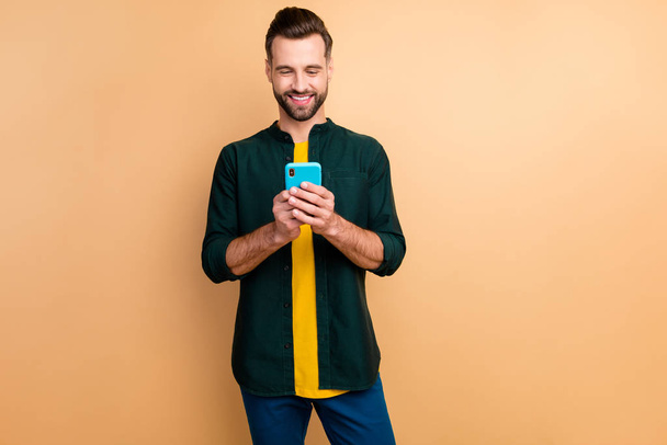 Photo of nice handsome hipster guy holding telephone hands good mood texting with friends speak over weekend meeting wear casual outfit isolated beige color background - Фото, зображення
