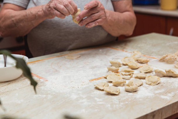 Mãos de mulher velha na cozinha esculpindo bolinhos
 - Foto, Imagem