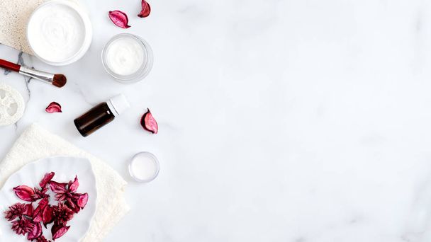 SPA natural organic cosmetic products on marble table. Top view hand cream jar, essential oil bottle, luffa sponge, towel, brush, rose petals. Minimal flat lay style composition. Skin care concept - 写真・画像