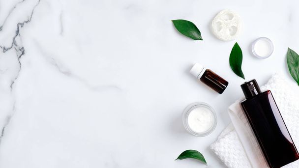 Natural organic cosmetic products and green leaves on marble background. Minimal flat lay style composition with essential oils, shampoo bottle, towel, hand cream. Body care, skincare concept - Zdjęcie, obraz