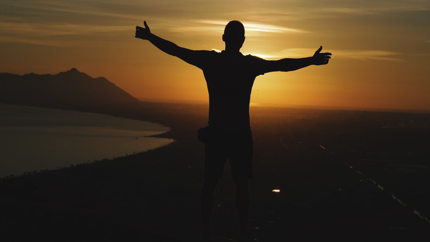 Ταξίδι. Ένας τύπος στέκεται στην κορυφή ενός βουνού και κοιτάζει το ηλιοβασίλεμα.. - Πλάνα, βίντεο