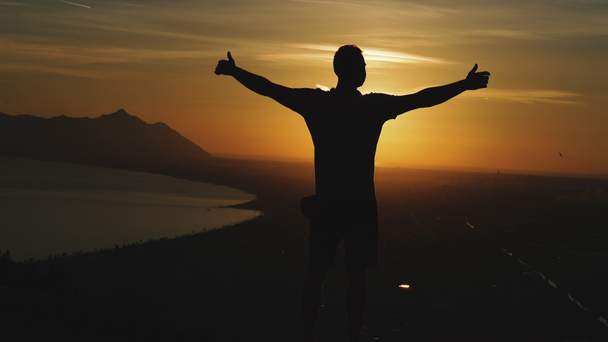 Voyage. Un gars se tient au sommet d'une montagne et regarde le coucher du soleil
. - Séquence, vidéo