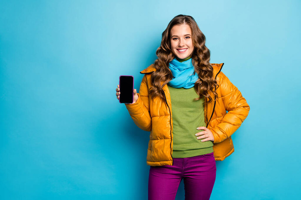 Photo of pretty lady hold telephone hands advising new gadget smart phone model low sale price wear yellow overcoat scarf violet trousers green jumper isolated blue color background - 写真・画像