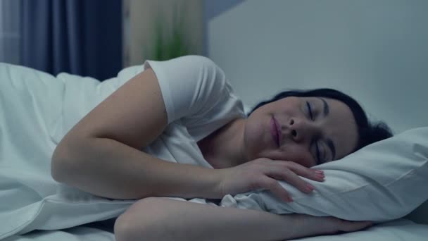 Relaxed young woman sleeping in bed at night, enjoying rest in home comfort - Materiał filmowy, wideo