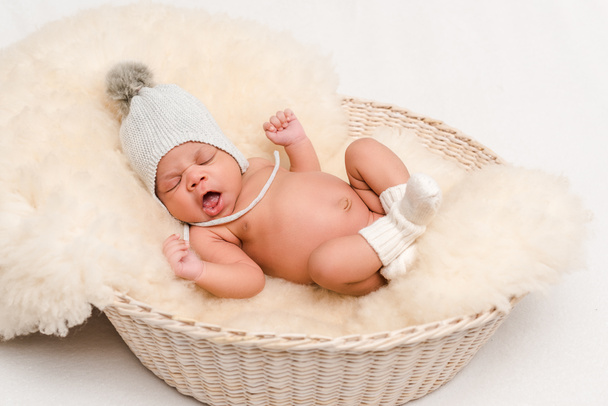  νεογέννητο μωρό μικτή φυλή σε πλεκτό καπέλο χασμουρητό στο καλάθι σε λευκό - Φωτογραφία, εικόνα