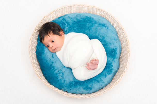 vista superior del bebé de raza mixta recién nacido envuelto en manta acostado en la cesta aislado en blanco
  - Foto, Imagen