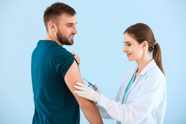 Γιατρός εμβολιάζει το νεαρό άνδρα σε ελαφρύ φόντο - Φωτογραφία, εικόνα