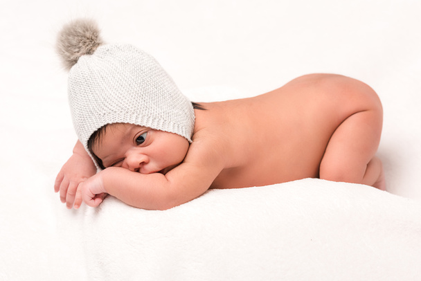 adorable mixto raza bebé en punto sombrero acostado en blanco
  - Foto, Imagen