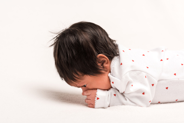 mixed race newborn in baby romper lying on white  - Фото, изображение