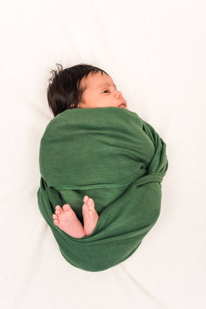 top view of bi-racial baby wrapped in green blanket lying on white  - Φωτογραφία, εικόνα