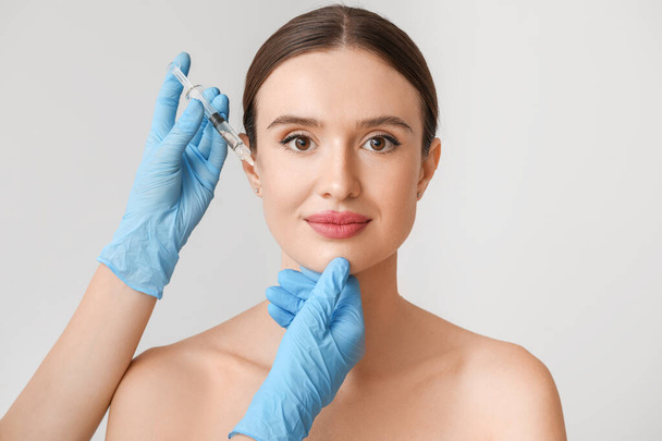 Young woman receiving filler injection against grey background - Foto, immagini