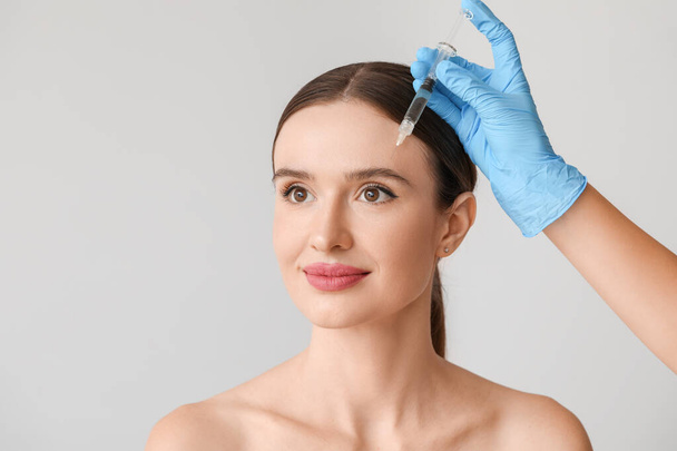 Young woman receiving filler injection against grey background - Foto, imagen