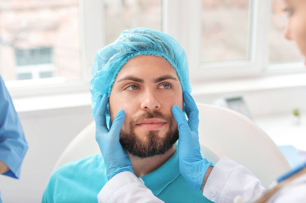 診療所で手術前に青年の顔を調べる整形外科医 - 写真・画像