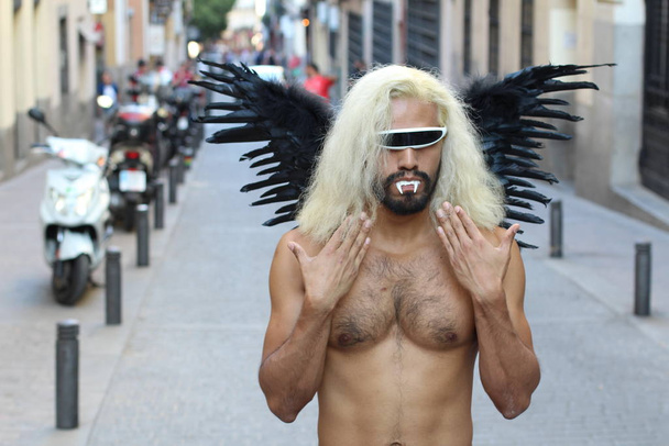 Shirtloze man met donkere vleugels en zonnebril die overdag buiten staat - Foto, afbeelding