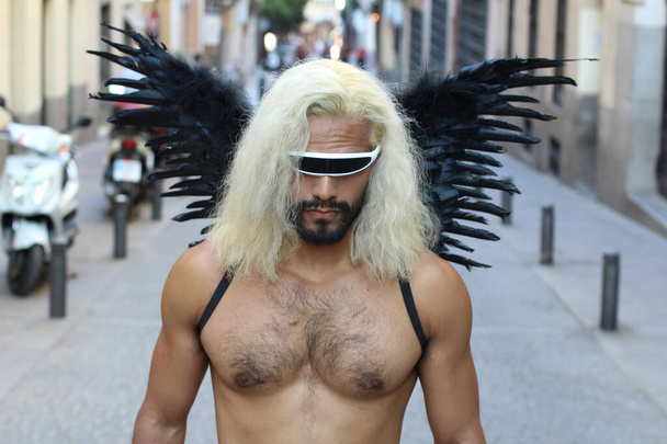Homme torse nu avec des ailes sombres et des lunettes de soleil debout à l'extérieur le jour
 - Photo, image