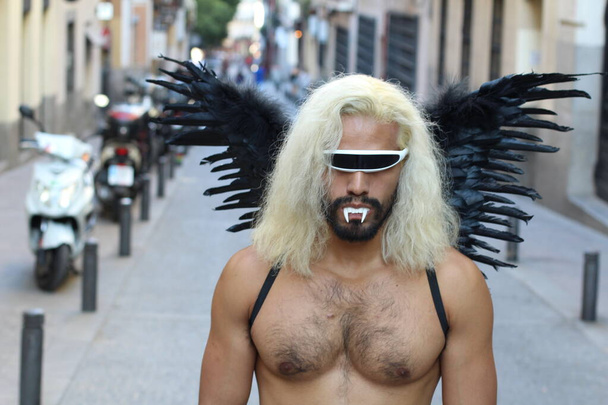 Shirtloze man met donkere vleugels en zonnebril die overdag buiten staat - Foto, afbeelding