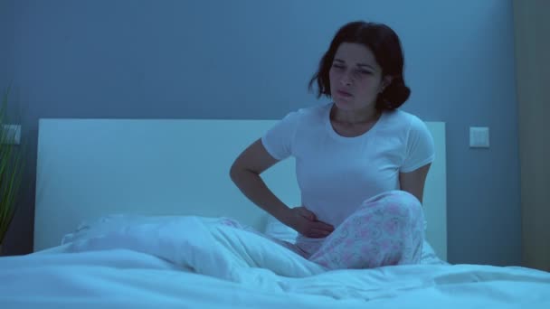 Unhappy woman having painful menstrual cramps, rubbing belly in bed at night - Video