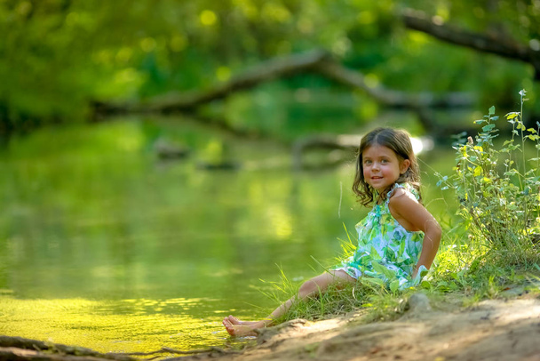 Chica de 4-5 años en un vestido verde y descalzo en el fondo del río en el bosque
 - Foto, imagen