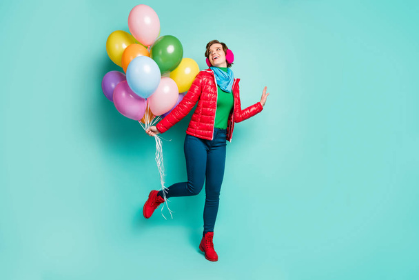 Full body photo of funny chilling lady came birthday party bring many colorful air balloons wear casual red coat scarf pink ear muffs pants shoes isolated teal color background - Foto, immagini