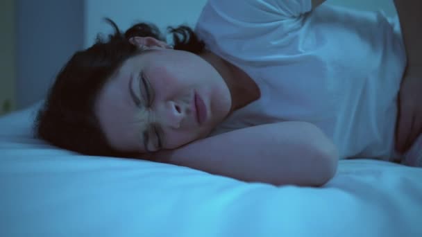 Sad female twisting with pain in stomach, lying on bed suffering painful cramps - Materiał filmowy, wideo